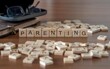 parenting word or concept represented by wooden letter tiles on a wooden table with glasses and a book