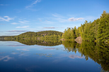 Wall Mural - Calm evening at the lake shore in Finland. Beautiful scenery with green leaves in the forest.