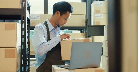 Asian business partner man wear formal shirt hold cardboard box use laptop computer check inventory online stock data program for delivery customer at warehouse. Startup small business concept.