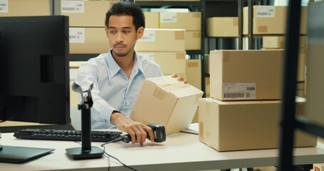 Wall Mural - Happy Asian man wear formal uniform shirt sit in front of desk use computer and barcode machine scanner record customer online data in cardboard box delivery at warehouse. Startup business concept.