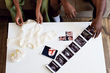 Couple With Baby Clothing And Ultrasound Pictures On Table