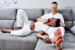© Westend61 - Young man lying on lap of happy boyfriend sitting on sofa at home