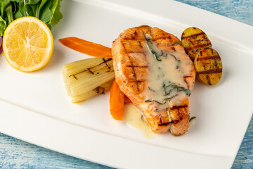 Grilled salmon in sauce with vegetables and potatoes on a white porcelain plate