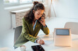 © Westend61 - Businesswoman talking on smart phone writing at desk in office