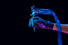Closeup Of Tattooer Master's Hand In Black Glove Holding Machine For Making Tattoo Art On Body Isolated On Dark Background In Neon Light.