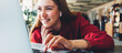 © Alex from the Rock - Happy pleased young woman in red sitting and looking at the screen of laptop, in big and bright open space
