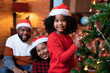 American family happy laughting celebrate christmas eve sitting at leather brown sofar in leaving room decoration with green christmas tree and lighting, daughter happy collect ball decorates and hang