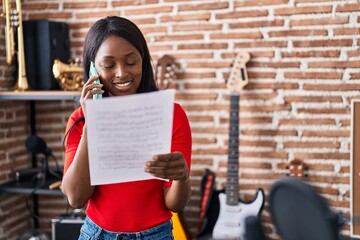 Sticker - Young african american woman musician talking on the smartphone reading music sheet at music studio