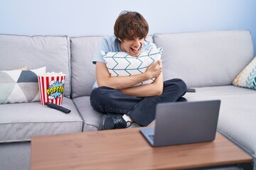 Canvas Print - Hispanic young man watching a horror movie in the laptop smiling and laughing hard out loud because funny crazy joke.