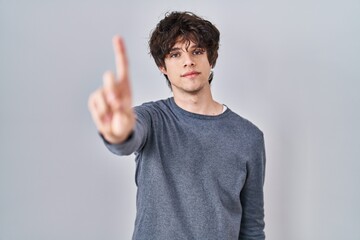 Sticker - Young man standing over isolated background pointing with finger up and angry expression, showing no gesture