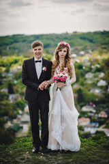 Wall Mural - Romantic couple newlyweds, bride and groom stands and holding bouquet of pink flowers and greens, greenery in the country. Wedding ceremony on nature.