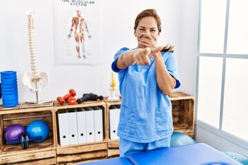 Sticker - Middle age hispanic physiotherapist woman working at pain recovery clinic laughing at you, pointing finger to the camera with hand over mouth, shame expression