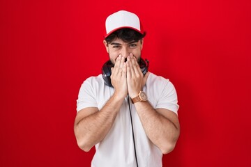 Sticker - Hispanic man with beard wearing gamer hat and headphones laughing and embarrassed giggle covering mouth with hands, gossip and scandal concept