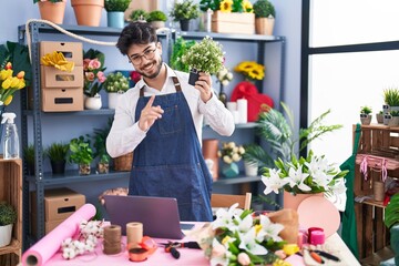 Wall Mural - Young hispanic man florist using laptop holding plant at florist shop