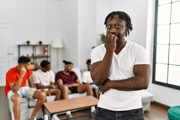 Poster - Young african man with friends at the living room looking stressed and nervous with hands on mouth biting nails. anxiety problem.