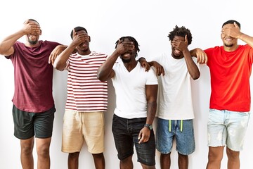 Poster - Young african group of friends standing together over isolated background smiling and laughing with hand on face covering eyes for surprise. blind concept.