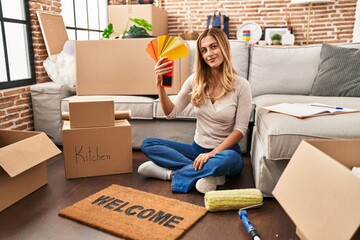 Poster - Young blonde woman choosing paint color at new home looking positive and happy standing and smiling with a confident smile showing teeth