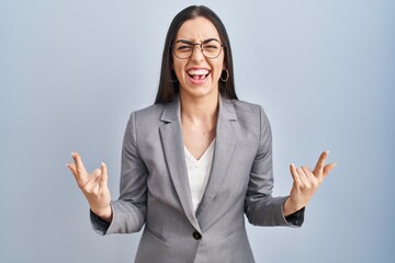 Sticker - Hispanic business woman wearing glasses shouting with crazy expression doing rock symbol with hands up. music star. heavy concept.