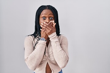 Sticker - African woman with braids standing over white background shocked covering mouth with hands for mistake. secret concept.