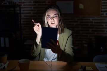 Poster - Blonde caucasian woman working at the office at night pointing aside worried and nervous with forefinger, concerned and surprised expression