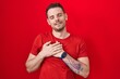 © Krakenimages.com - Young hispanic man standing over red background smiling with hands on chest with closed eyes and grateful gesture on face. health concept.