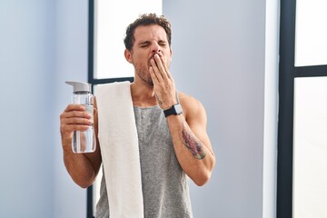 Poster - Young hispanic man wearing sportswear drinking water bored yawning tired covering mouth with hand. restless and sleepiness.