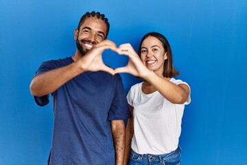 Poster - Young hispanic couple standing together smiling in love doing heart symbol shape with hands. romantic concept.