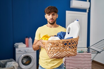 Wall Mural - Arab man with beard holding laundry basket and detergent bottle skeptic and nervous, frowning upset because of problem. negative person.