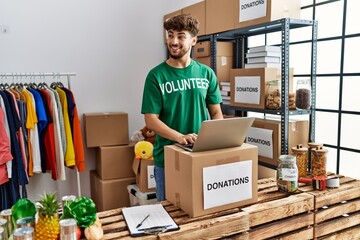 Sticker - Young arab man wearing volunteer uniform using laptop at charity center