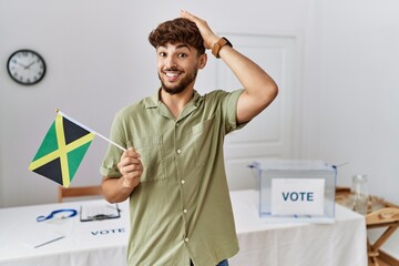 Sticker - Young arab man at political campaign election holding jamaica flag stressed and frustrated with hand on head, surprised and angry face