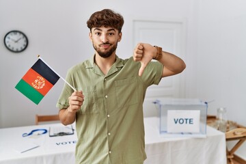 Poster - Young arab man at political campaign election holding afghanistan flag with angry face, negative sign showing dislike with thumbs down, rejection concept