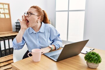 Poster - Young redhead woman working at the office using computer laptop shouting and screaming loud to side with hand on mouth. communication concept.