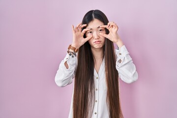 Sticker - Chinese young woman standing over pink background trying to open eyes with fingers, sleepy and tired for morning fatigue