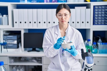 Wall Mural - Chinese young woman working at scientist laboratory mixing skeptic and nervous, frowning upset because of problem. negative person.