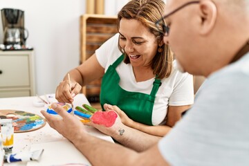 Middle age hispanic painter couple smiling happy painting palm hands at art studio.