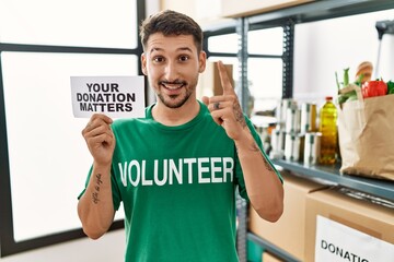 Sticker - Young volunteer man holding your donation matters banner surprised with an idea or question pointing finger with happy face, number one