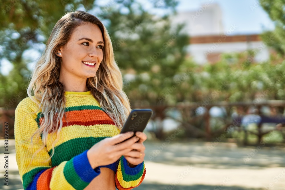 Young blonde woman using smartphone at the park