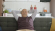 Elderly man slumping into armchair and clasping his hands behind his head in his peaceful home. Portrait of happy old man in his peaceful home.
