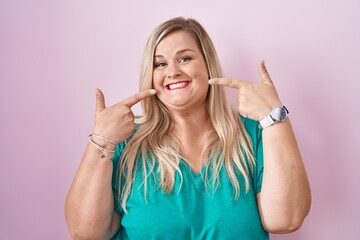 Sticker - Caucasian plus size woman standing over pink background smiling cheerful showing and pointing with fingers teeth and mouth. dental health concept.