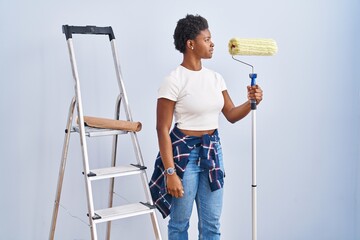 Wall Mural - African american woman holding roller painter looking to side, relax profile pose with natural face and confident smile.