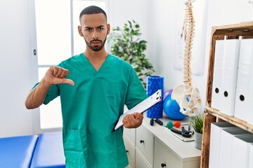 Poster - African american physiotherapist man working at pain recovery clinic pointing down looking sad and upset, indicating direction with fingers, unhappy and depressed.