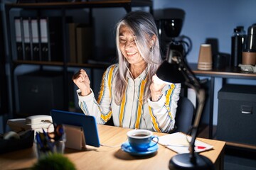 Sticker - Middle age woman with grey hair working at the office at night celebrating surprised and amazed for success with arms raised and open eyes. winner concept.