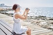 © Krakenimages.com - Young caucasian girl using professional camera sitting on the bench at the beach.