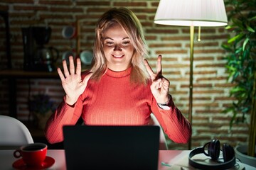 Canvas Print - Blonde woman using laptop at night at home showing and pointing up with fingers number seven while smiling confident and happy.