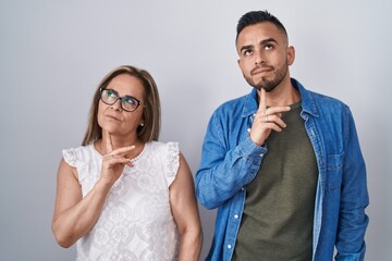 Wall Mural - Hispanic mother and son standing together thinking concentrated about doubt with finger on chin and looking up wondering