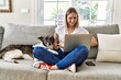 Young caucasian girl smiling happy sitting on the sofa with dog using laptop at home.