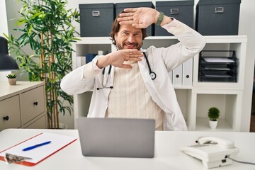 Canvas Print - Handsome middle age doctor man working at the clinic smiling cheerful playing peek a boo with hands showing face. surprised and exited