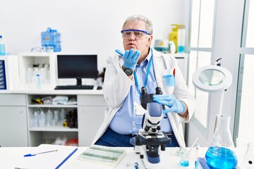 Wall Mural - Senior caucasian man working at scientist laboratory looking at the camera blowing a kiss with hand on air being lovely and sexy. love expression.