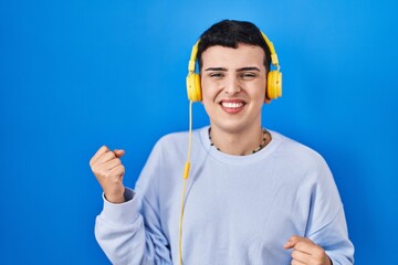 Sticker - Non binary person listening to music using headphones very happy and excited doing winner gesture with arms raised, smiling and screaming for success. celebration concept.