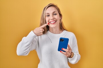 Canvas Print - Young blonde woman using smartphone typing message smiling cheerful showing and pointing with fingers teeth and mouth. dental health concept.